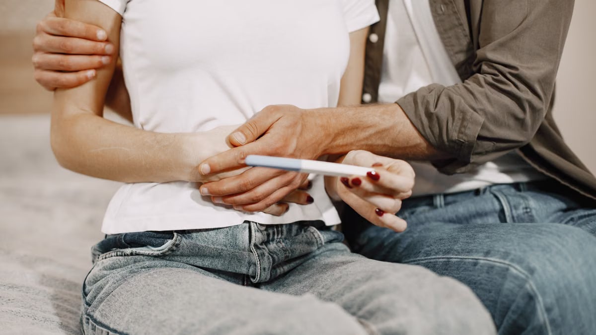 A couple joyfully embraces while holding a positive pregnancy test at home.